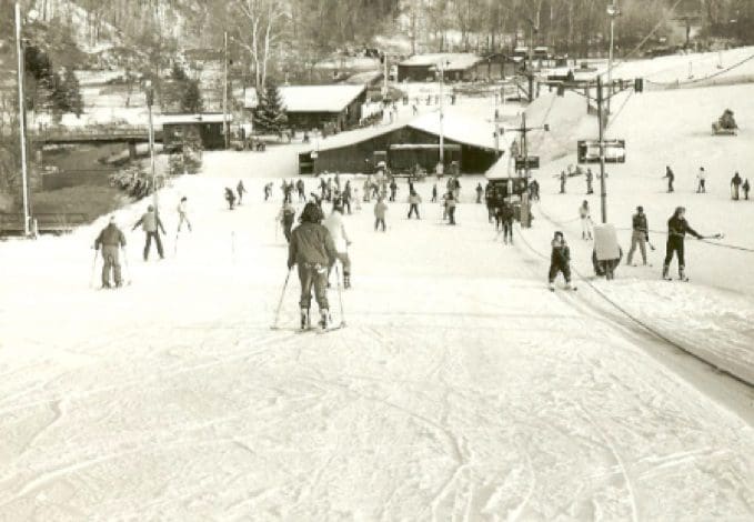 People skiing and walking on a snowy slope near a ski lodge.