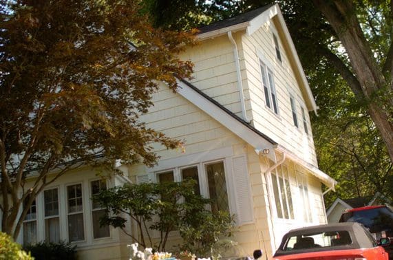 Yellow house with trees and red car.