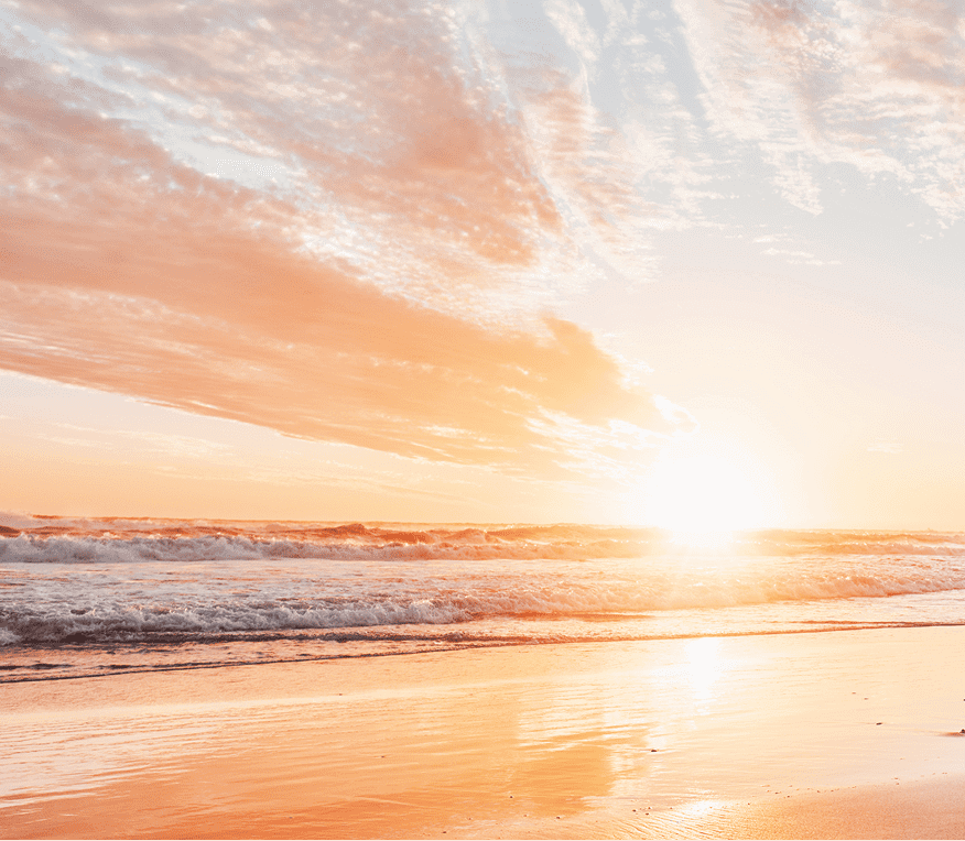 Sunset over the ocean with sandy beach.