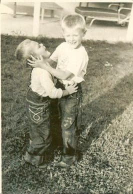 Two young boys playing and hugging outside.
