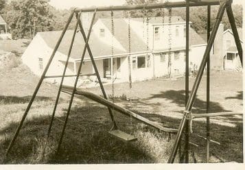 Old swing set with house in background.