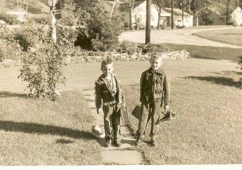 Two boys in vintage cowboy costumes outside.