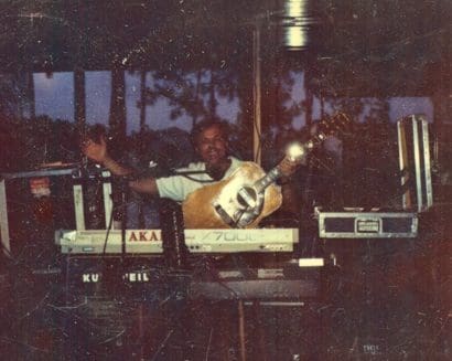 Musician playing guitar and keyboards on stage.