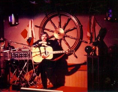 Musician playing guitar on nautical-themed stage.