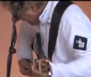 Musician playing guitar in white jacket.