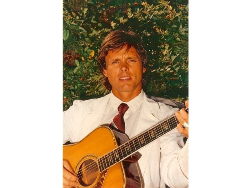 Man in suit playing acoustic guitar outdoors.