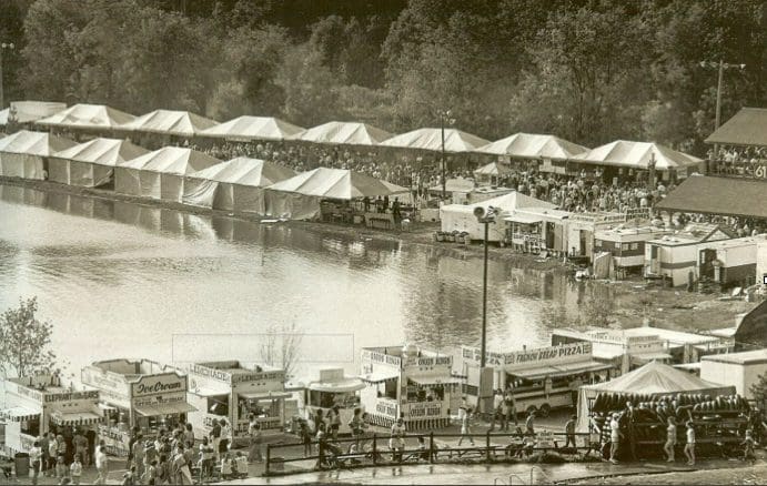 Outdoor festival with tents by a lake.