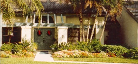 A charming house entrance decorated with wreaths and surrounded by greenery and flowers.