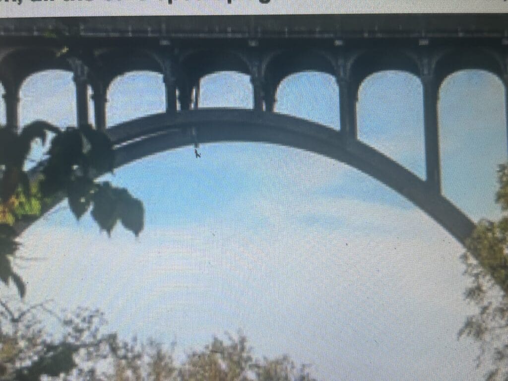 An arch bridge with cars passing over it against a blue sky.