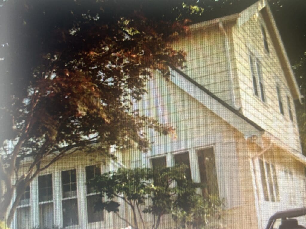A house with a large tree casting shadows over the roof and porch.