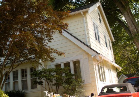 Yellow house with trees and red car.