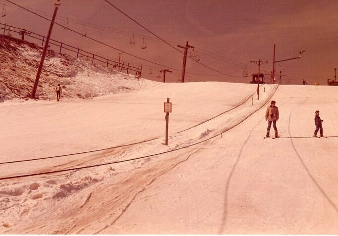 Skiers on snowy slope with ski lift.