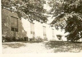 Old building surrounded by trees and grass.
