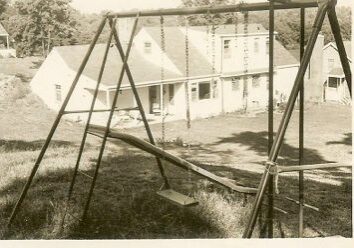 Old swing set with house in background.
