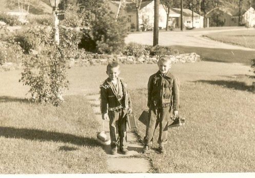 Two boys in vintage cowboy costumes outside.