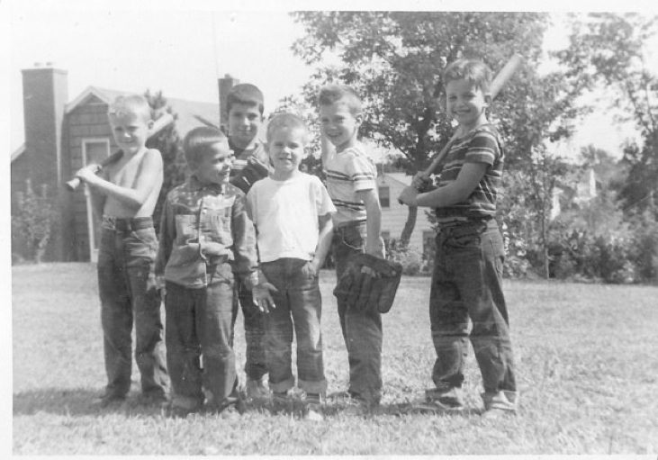 Six boys posing with baseball equipment outside.