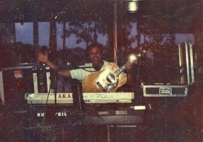 Musician playing guitar and keyboards on stage.