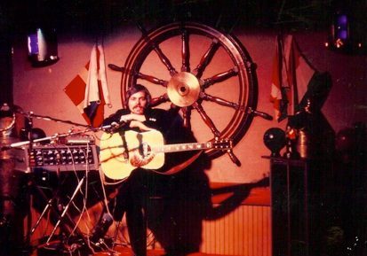 Musician playing guitar on nautical-themed stage.