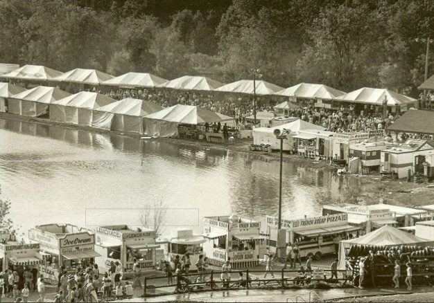 Outdoor festival with tents by a lake.
