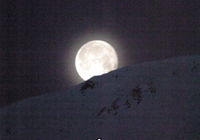 Full moon rising over snowy mountain.